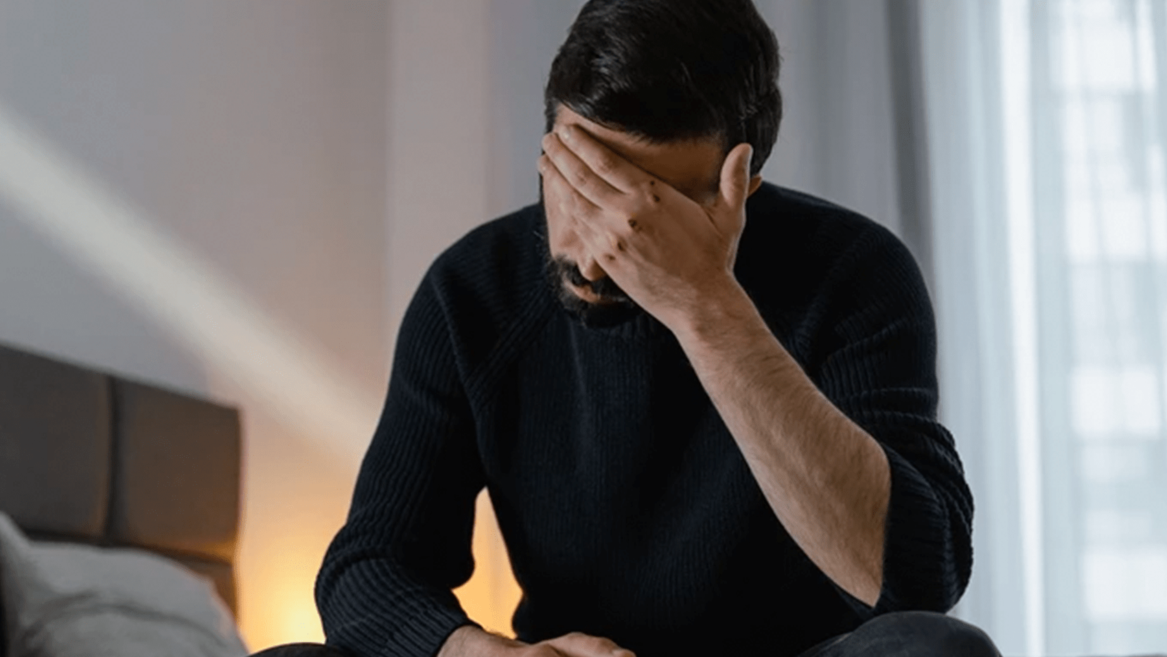 Man sitting on bed with hand on forehead