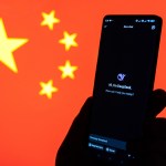 A hand holding a phone showing the DeepSeek app with the Chinese flag in the background.