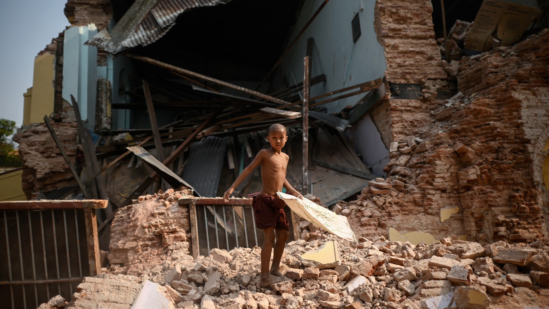 A young monk standing in front of a ruined building.